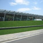 Modern Exterior of Tiriana International airport in Albania, with blue skies in the background and a green lawn in front of the terminal.