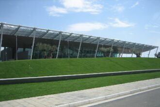 Modern Exterior of Tiriana International airport in Albania, with blue skies in the background and a green lawn in front of the terminal.