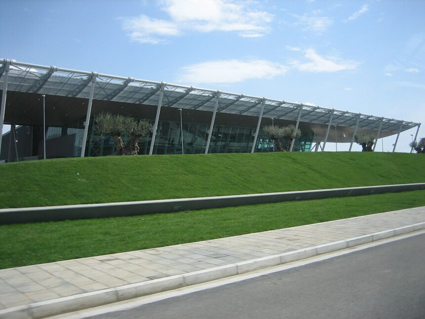 Modern Exterior of Tiriana International airport in Albania, with blue skies in the background and a green lawn in front of the terminal.