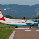 An Austrian Arrows Bombardier Dash 8 Q400 aircraft taxiing on a runway with mountains in the background.