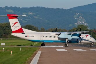 An Austrian Arrows Bombardier Dash 8 Q400 aircraft taxiing on a runway with mountains in the background.