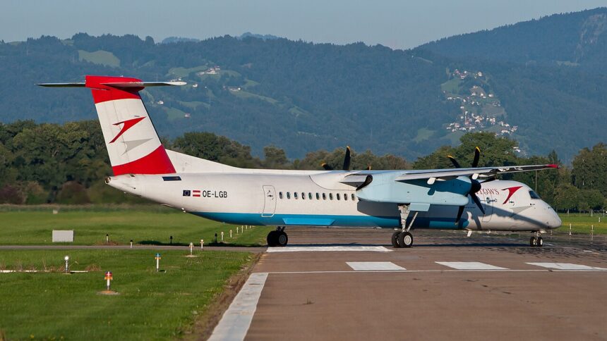 An Austrian Arrows Bombardier Dash 8 Q400 aircraft taxiing on a runway with mountains in the background.