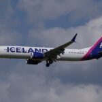 Icelandair B737-9 flying under a cloudy sky, but with some blue peeking through the clouds. The livery is mostly white, but it has pink and dark blue accents.