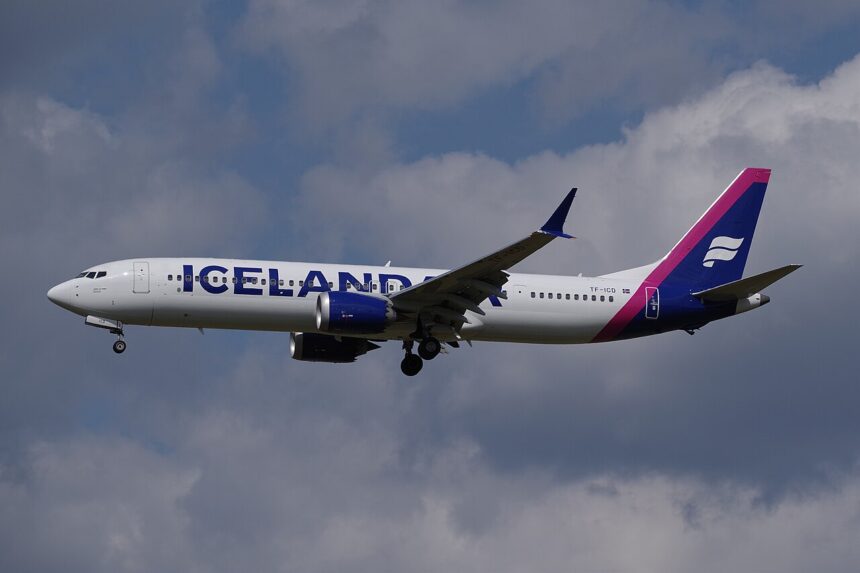 Icelandair B737-9 flying under a cloudy sky, but with some blue peeking through the clouds. The livery is mostly white, but it has pink and dark blue accents.
