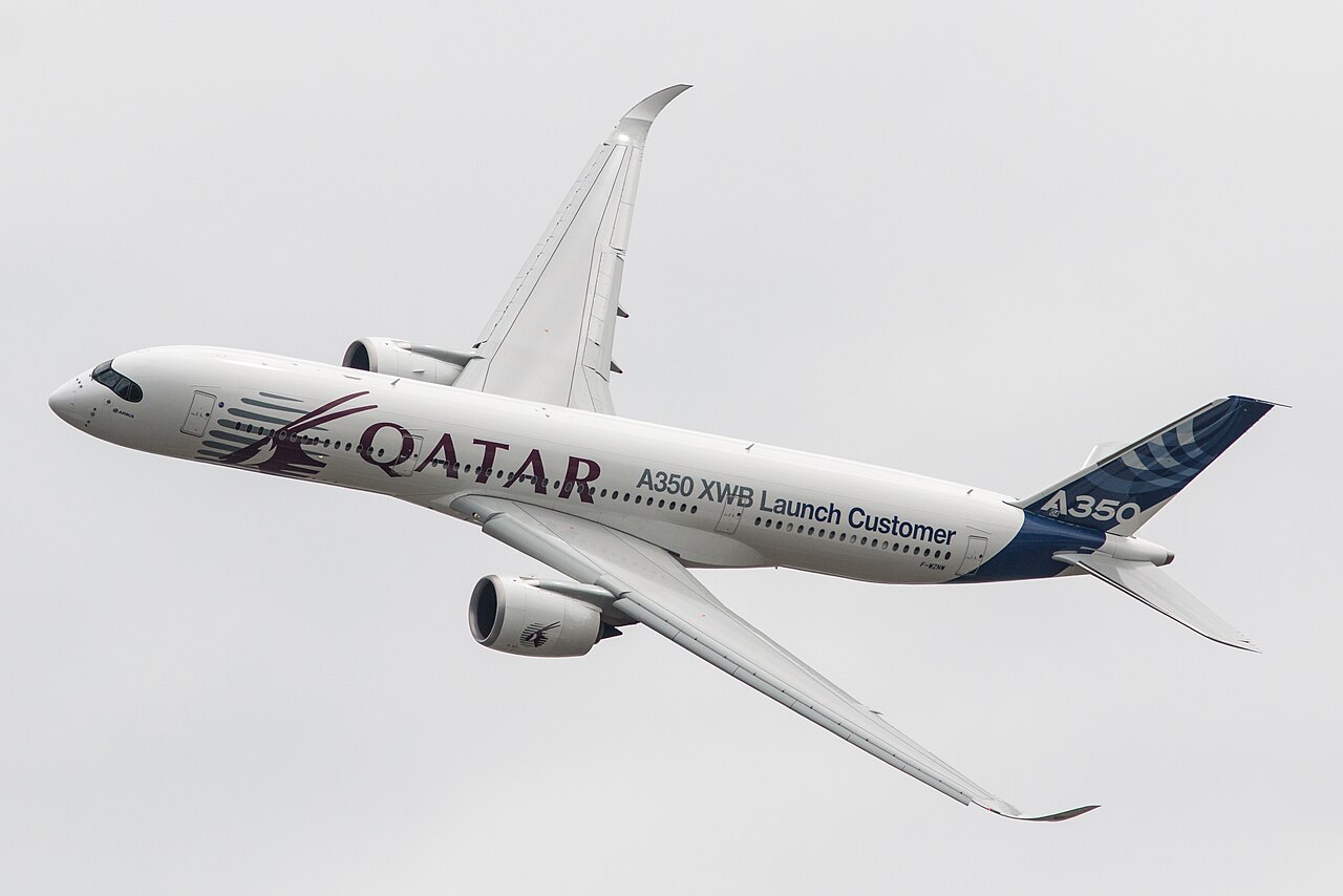 A Qatar Airways A350 flying under a grey sky. Its livery red, white, grey and blue.