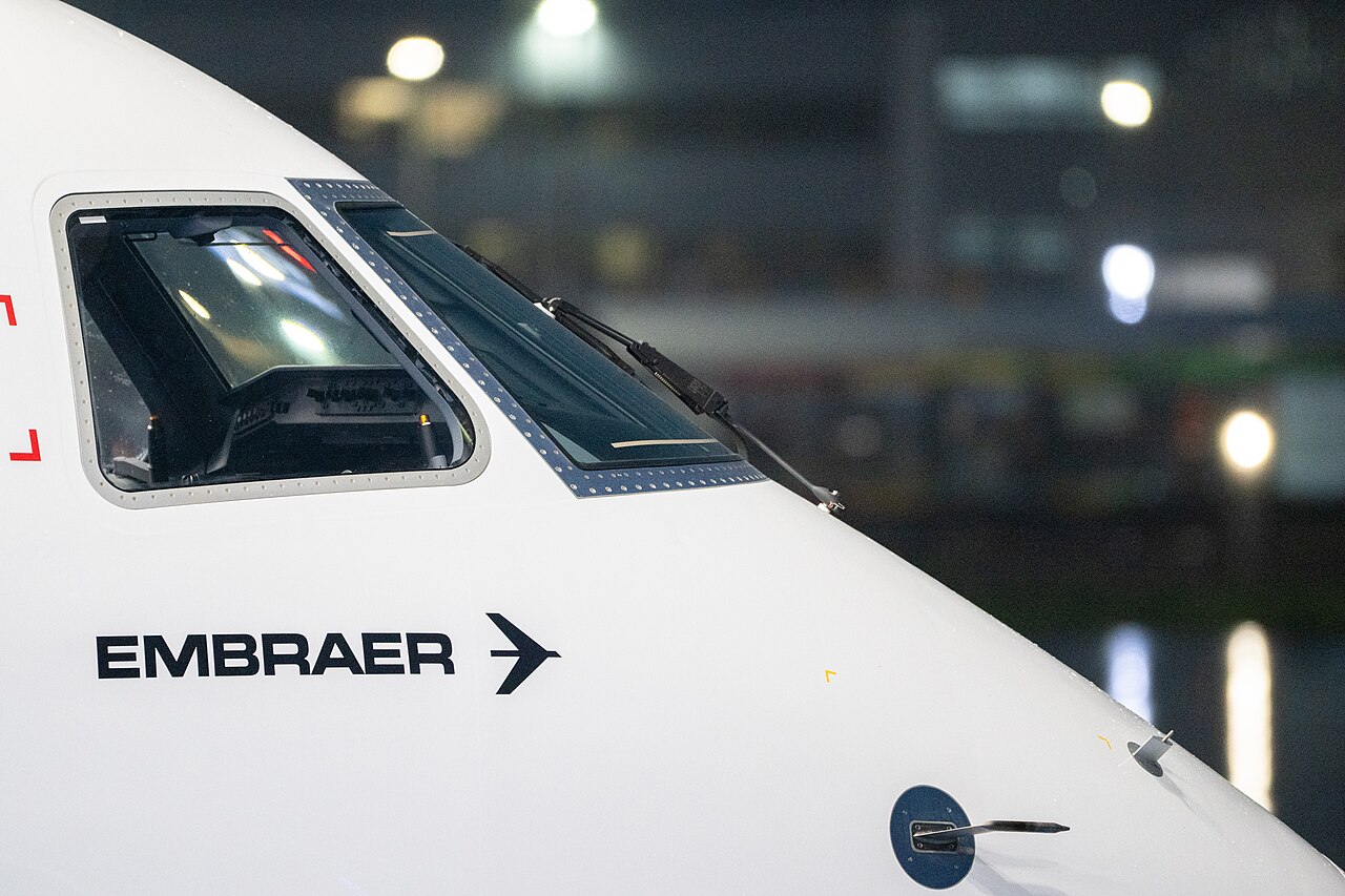 Head-on view of an Embraer E195-E2 aircraft parked on an airport apron, showing the cockpit, nose section, and twin engines under the wings.
