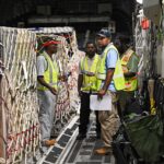 Military cargo aircraft and personnel participate in a large-scale logistics and air mobility exercise on an airport tarmac.