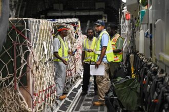 Military cargo aircraft and personnel participate in a large-scale logistics and air mobility exercise on an airport tarmac.