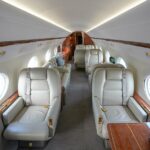 Luxury interior of a Gulfstream G450 private jet featuring cream leather seats, wood trim and spacious seating arrangements.