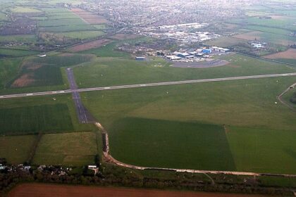 View of a runway and surrounding airfield buildings at London Oxford Airport under a clear sky.