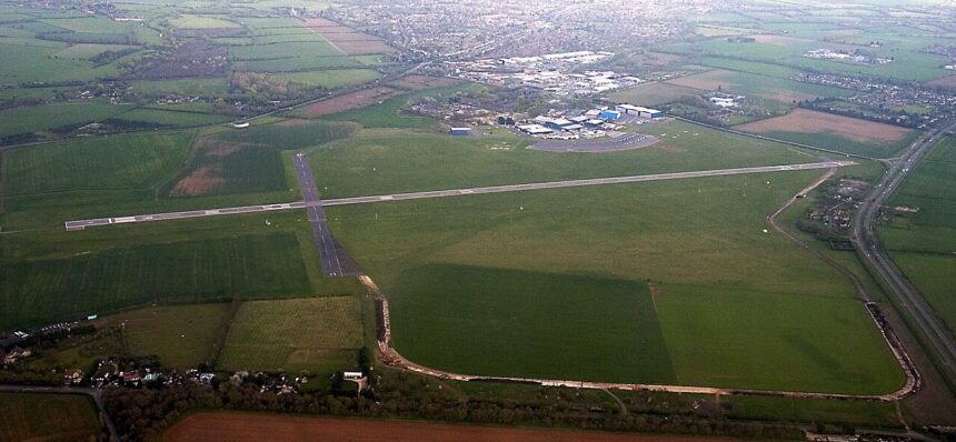 View of a runway and surrounding airfield buildings at London Oxford Airport under a clear sky.
