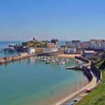Colourful houses overlook Tenby Harbour in Pembrokeshire, Wales, with fishing boats resting in the harbour at low tide.