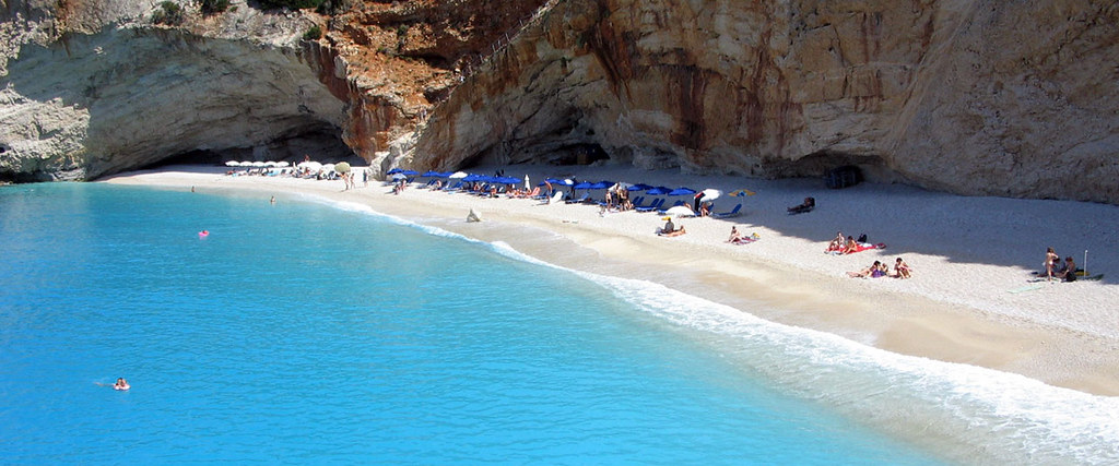 White sandy beach on Lefkada with towering white limestone cliffs rising behind clear blue sea.