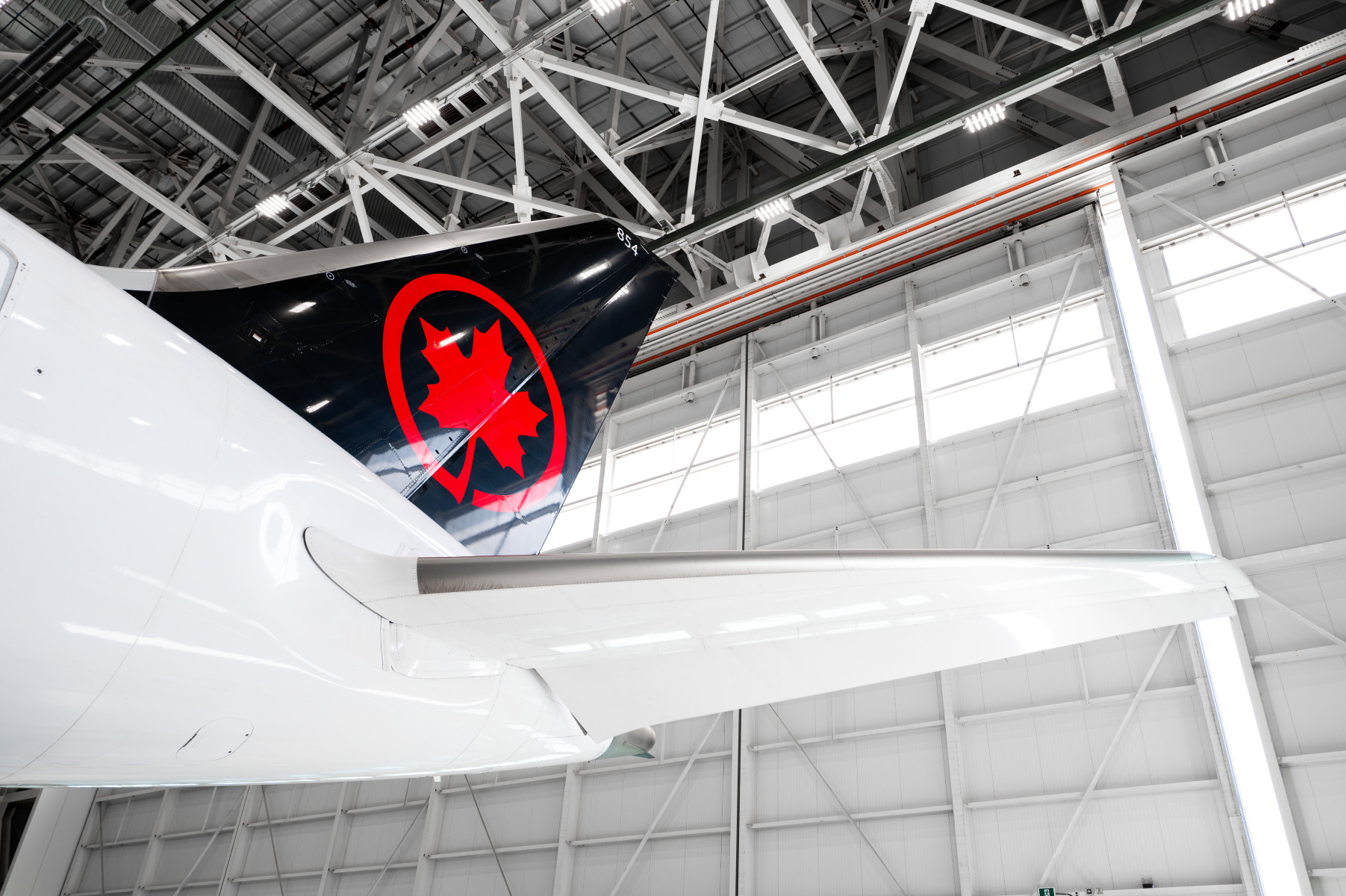 The tail of an Air Canada Boeing 787, inside an aircraft hangar. Black tail with a red maple leaf inside of a red circle.