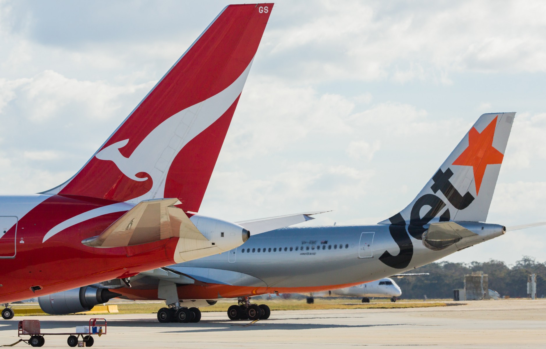 Jetstar and Qantas aircraft tails on the taxiway. Jetstar has grey, black and orange livery, while Qantas has red and white with a kangaroo on the tail.