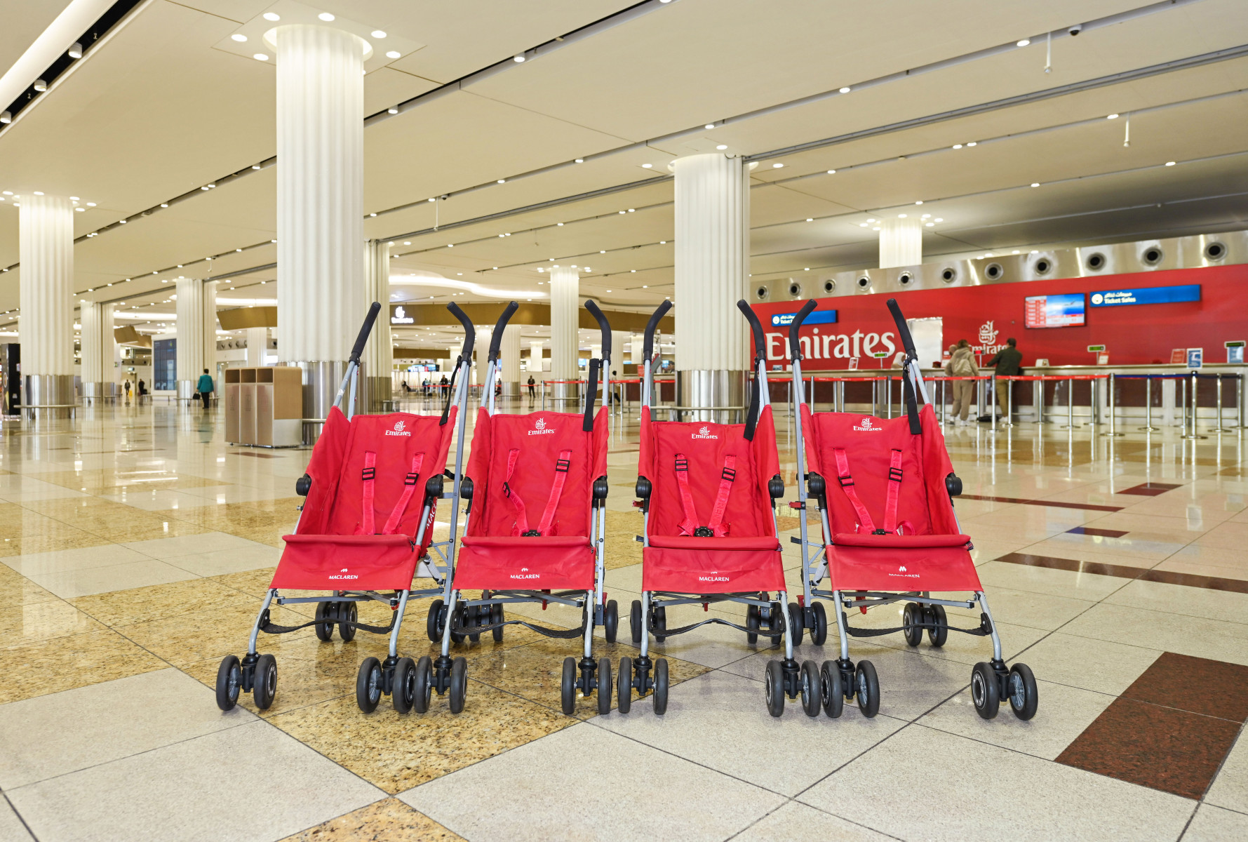 Four red strollers positioned next to each other in an airport