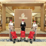 Three female Emirates staff stand behind three red strollers