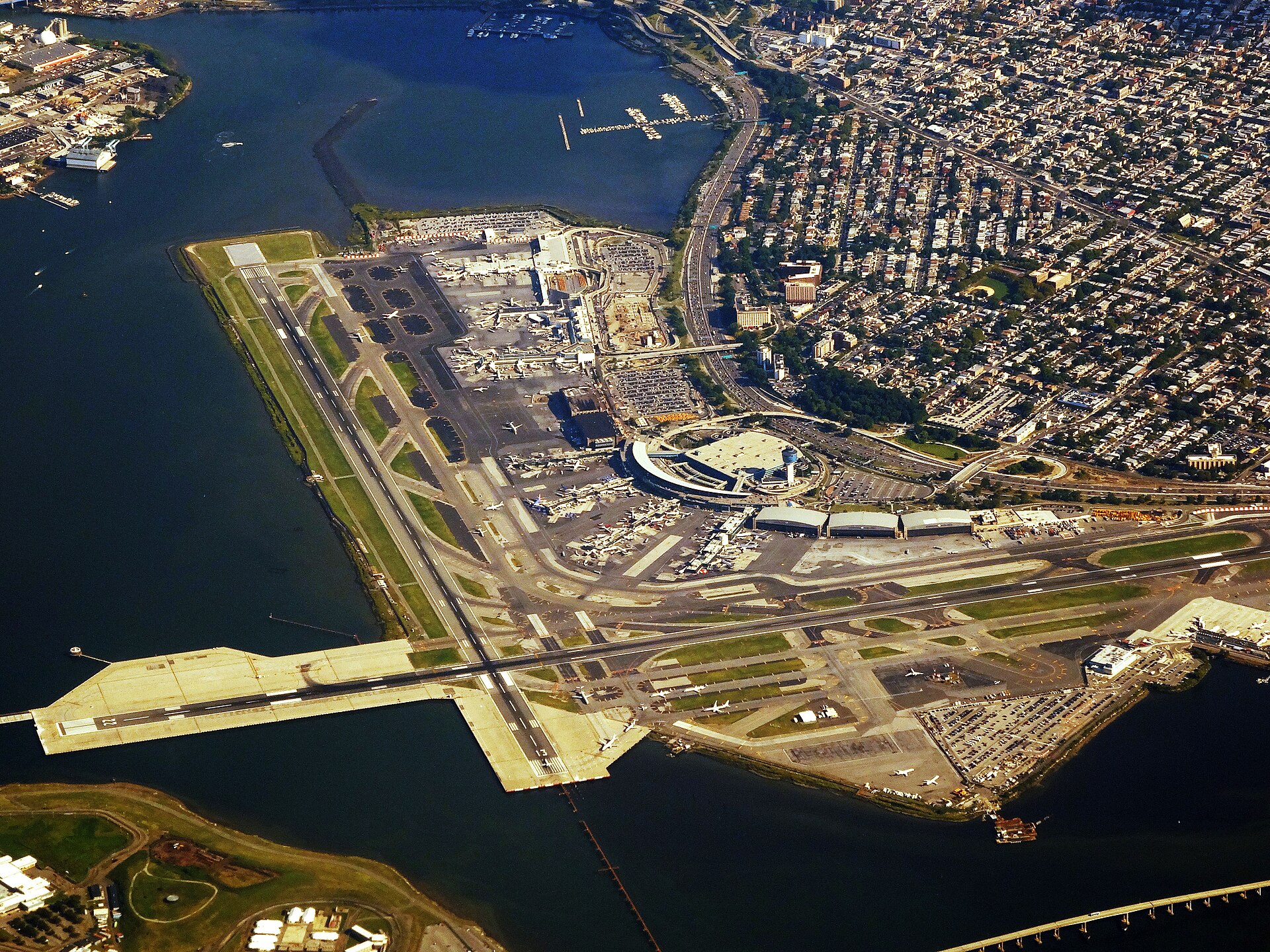 Aerial image of LaGuardia airport. the airport is in the centre, with very blue water surrounding it in a C shape from upper left corner to lower right.