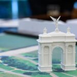 A small model arch is positioned on a colour map of Washington DC in a meeting room. The background is stylistically blurred, making the small white model arch the key focus of the picture.
