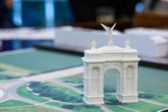 A small model arch is positioned on a colour map of Washington DC in a meeting room. The background is stylistically blurred, making the small white model arch the key focus of the picture.