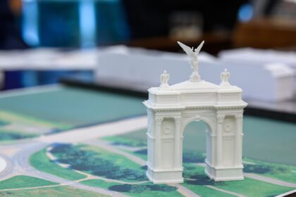 A small model arch is positioned on a colour map of Washington DC in a meeting room. The background is stylistically blurred, making the small white model arch the key focus of the picture.