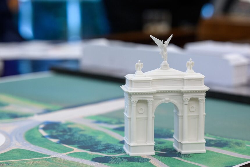 A small model arch is positioned on a colour map of Washington DC in a meeting room. The background is stylistically blurred, making the small white model arch the key focus of the picture.
