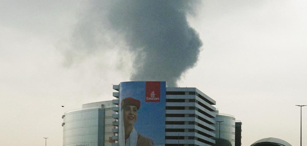 Fire at Dubai Airport after being hit by a drone attack. smoke rising from the building behind an Emirates billboard.