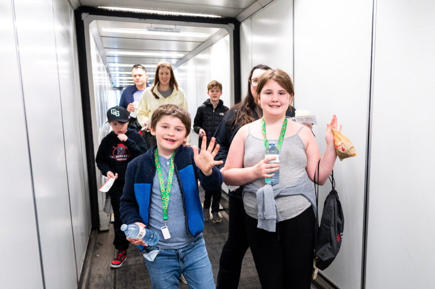 Children waving at the camera as they board the plane to experience a replication of aircraft procedures.