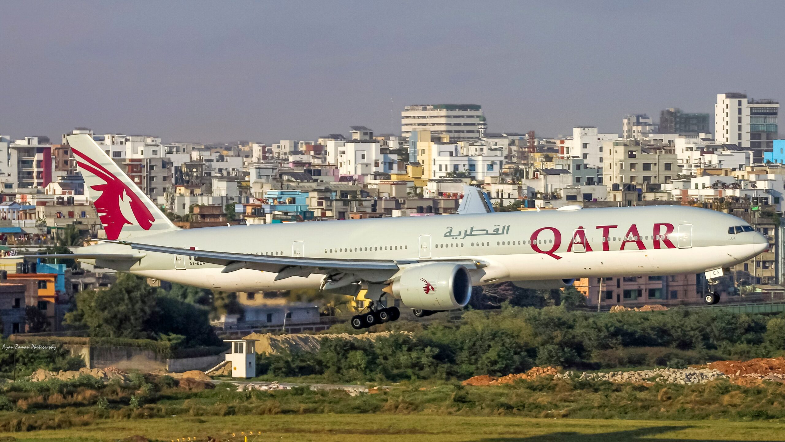 Qatar Airways Boeing 777 taking off against a backdrop of apartment blocks and towers 