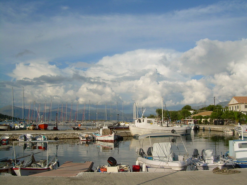 Small boats moored in the peaceful harbour of Kastos Island, Greece, surrounded by traditional waterfront buildings and clear blue water.