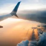 Looking out of the aircraft window, aircraft wing in view, flying through the clouds during an orange sunset.