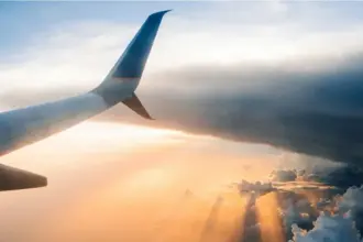 Looking out of the aircraft window, aircraft wing in view, flying through the clouds during an orange sunset.