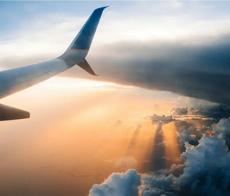 Looking out of the aircraft window, aircraft wing in view, flying through the clouds during an orange sunset.