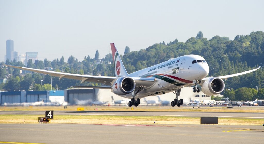 Biman Bangladesh Airlines Boeing 787 taking off from the runway. White, green and red livery. Trees and buildings seen in the background.