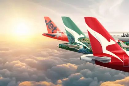 Tails of Qantas group aircraft- Qantas and Jetstar, mid-flight. Clouds beneath them, the sun in the background.