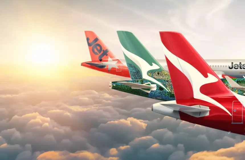 Tails of Qantas group aircraft- Qantas and Jetstar, mid-flight. Clouds beneath them, the sun in the background.