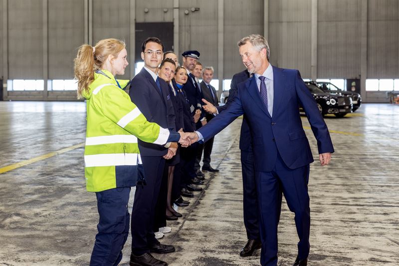 King Frederik X shakes hands with a lady in a reflective jacket in an aircraft hanger
