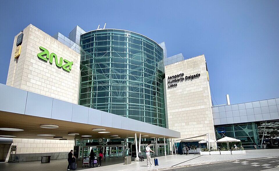 Lisbon Airport in Portugal, taken in August 2021. Blue sky in the background, passengers with suitcases shown in the foreground.