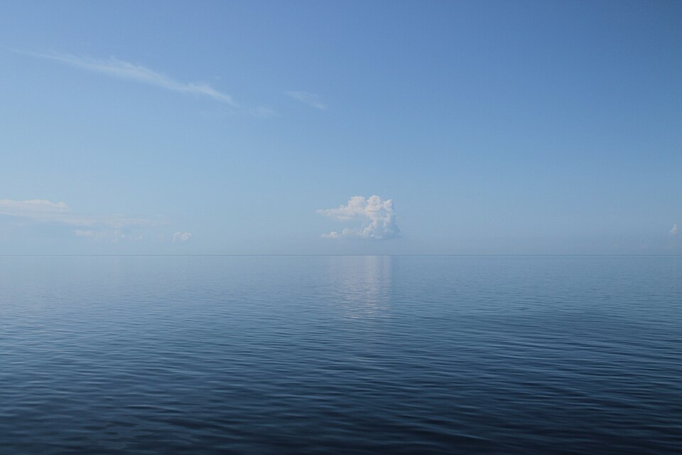 Calm waters of the Baltic Sea beneath a clear blue sky with distant white clouds along the horizon.