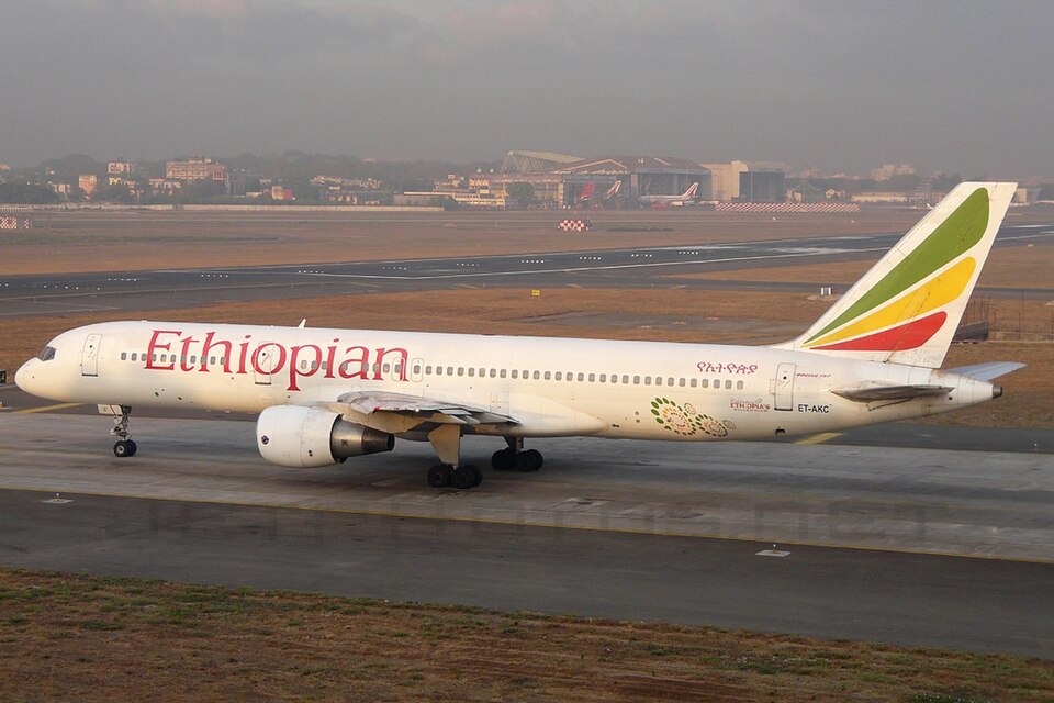 An Ethiopian Airlines B757 on the ground at Mumbai Airport. The sky is grey, as well as the runway. Its livery is mostly white with green, yellow, and red accents on its tail.