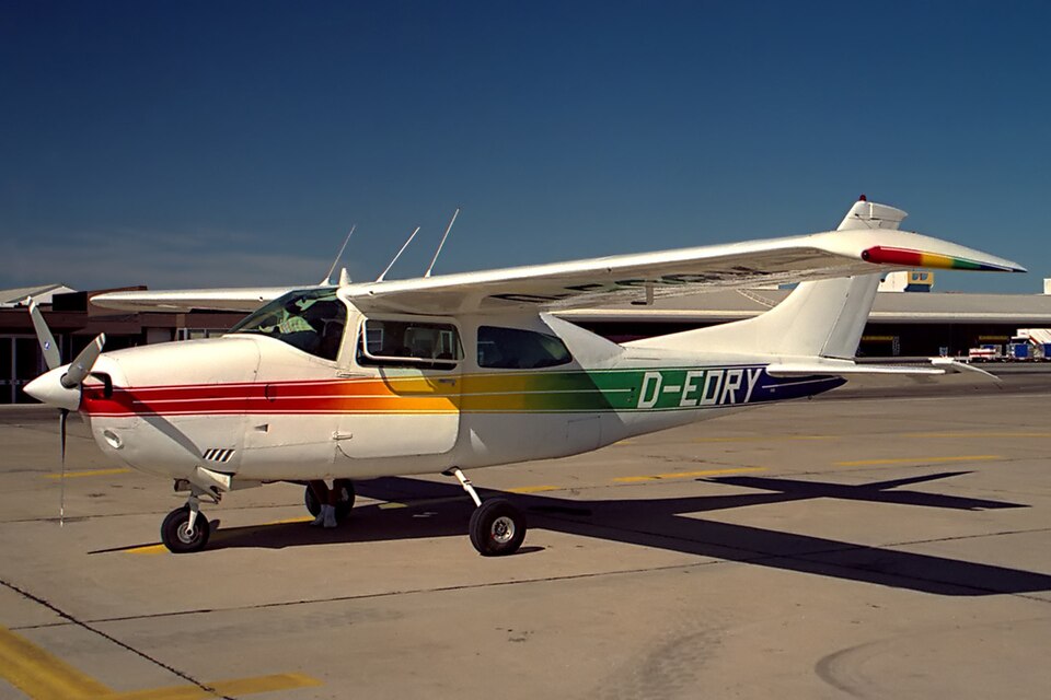 A rainbow-striped Cessna 210 Centurion parked on a sunlit airport tarmac. The single-engine aircraft is representative of the type involved in the fatal crash in Nuevo León, Mexico.