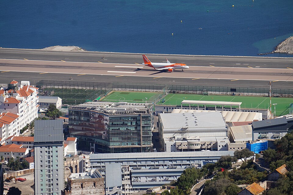 Aerial view of an easyJet aircraft taxiing on the runway at Gibraltar International Airport next to the sea and nearby city buildings.