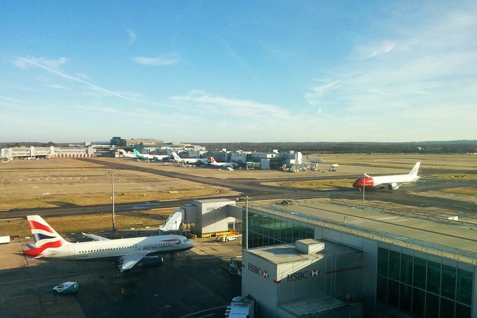 View of London Gatwick Airport showing terminal buildings and surrounding airfield infrastructure. Aircraft are shown in the foreground and background.
