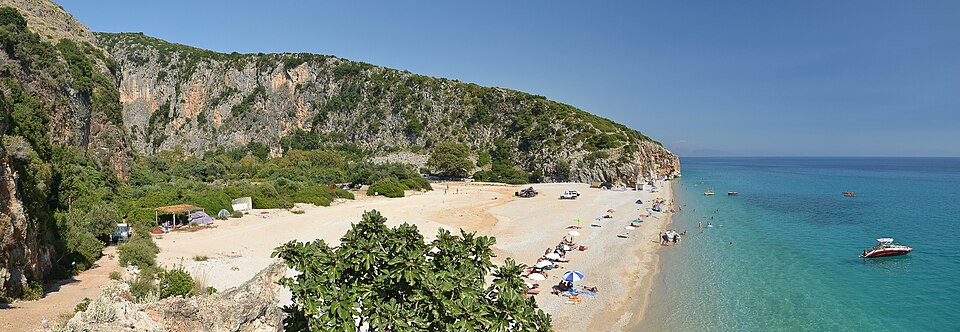 Gjipe Beach in Albania, featuring turquoise waters, rocky cliffs, and a narrow pebbled shoreline.