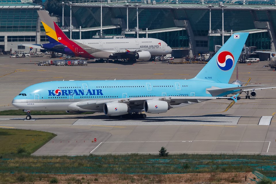 A Korean Air Airbus A380 moves across the runway at Incheon International Airport while an Asiana Airlines Airbus A380 sits at the terminal, symbolising the two South Korean carriers ahead of their landmark merger in late 2026.