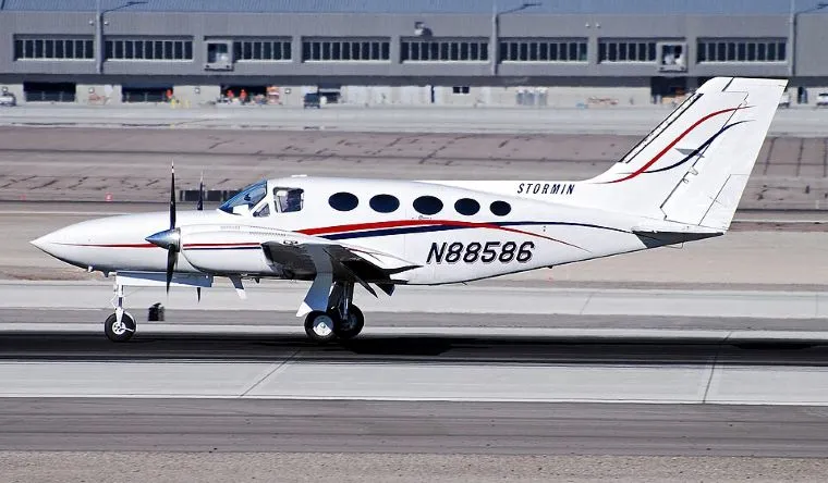 Small twin-engine propeller aircraft, registered N88586, white fuselage with red and blue stripes. On the tarmac before takeoff.