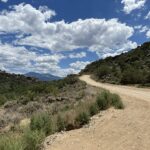 A dusty road cuts through mountainous countryside beneath scattered clouds. The image reflects the isolated and difficult terrain of Santiago, Nuevo León, where rescue crews responded to the deadly plane crash.