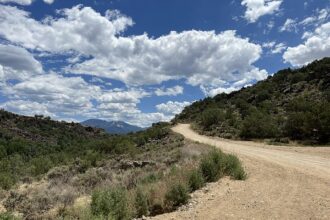 A dusty road cuts through mountainous countryside beneath scattered clouds. The image reflects the isolated and difficult terrain of Santiago, Nuevo León, where rescue crews responded to the deadly plane crash.