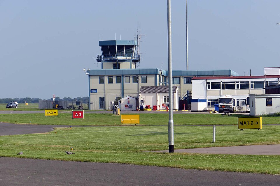 Air traffic control tower building. Grass in the foreground, grey-ish sky in the background.