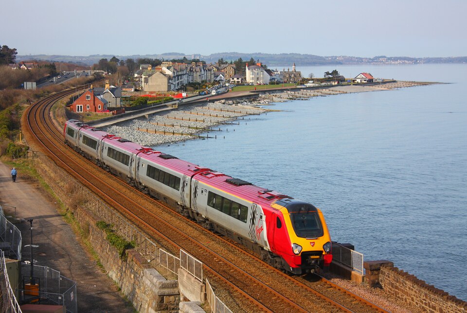Passenger train travelling along a coastal railway line near Llanfairfechan, with sea and hills in the background.